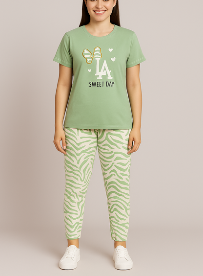 A woman wearing a green pajama set with a short-sleeve top that has a graphic design and the text 'LA SWEET DAY', paired with full-length pants with an all-over animal print. She is standing against a white background.